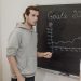 Three professionals engaged in a business discussion about goals written on a chalkboard in an office.